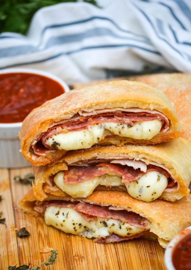 three meat & cheese stromboli slices stacked on a wooden cutting board
