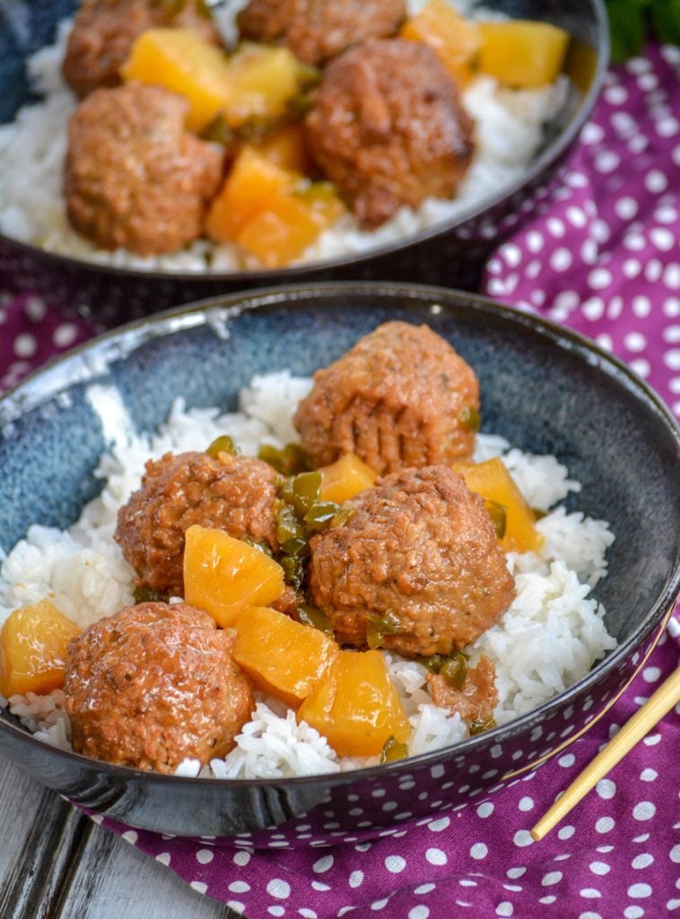 Crockpot Hawaiian Meatballs over a bed of rice in glazed bowls on top of a purple napkin