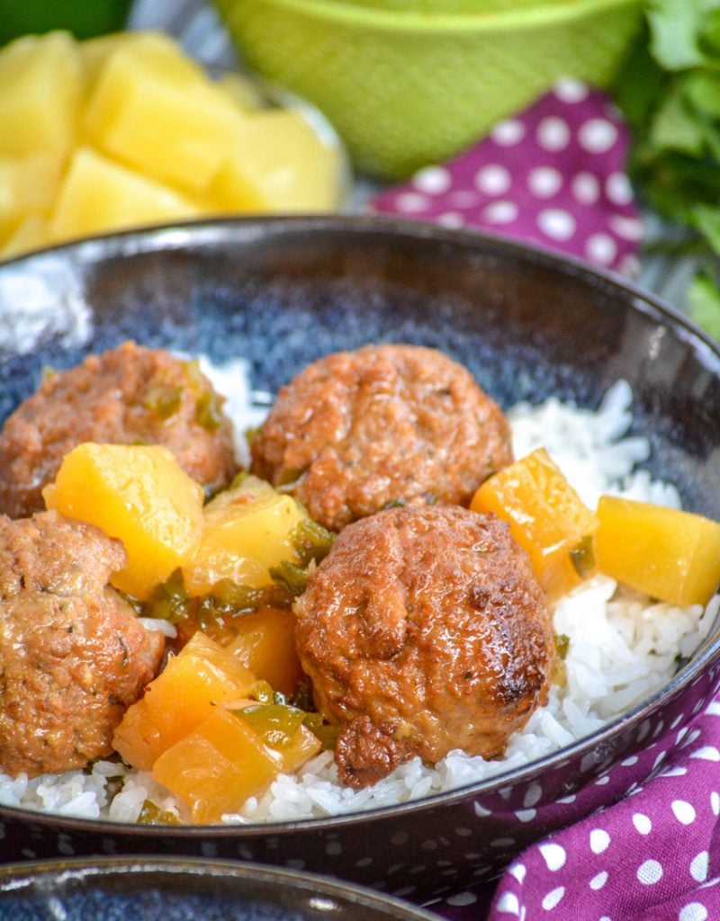 Crockpot Hawaiian Meatballs over a bed of rice in glazed bowl on a purple napkin with fresh pineapple in the background