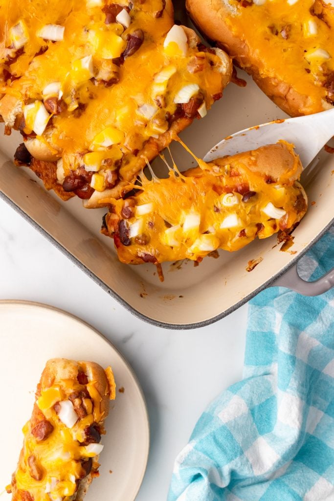 baked hot dogs in a casserole dish with a white spatula nestled underneath