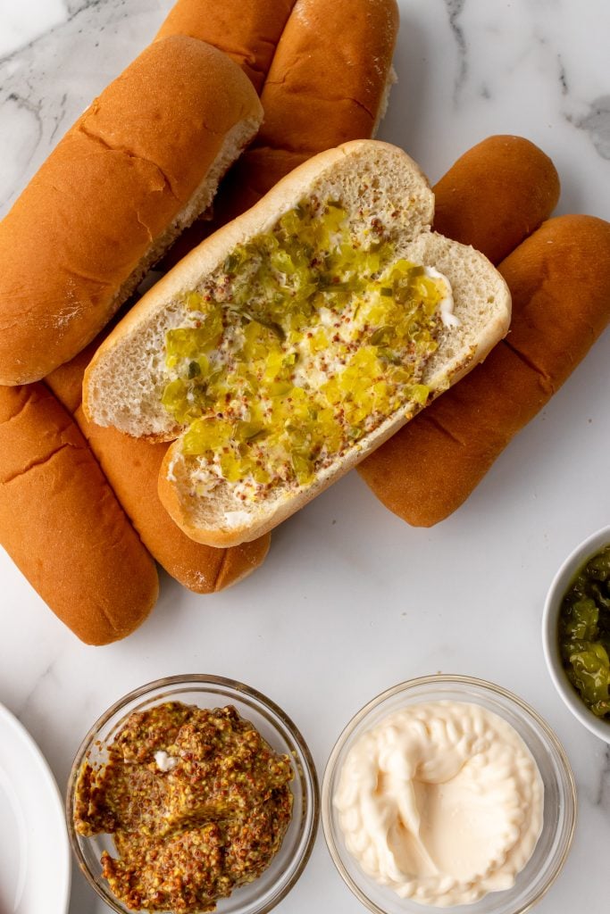 an open hot dog bun spread with mayonnaise, mustard, and relish
