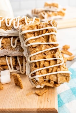 a stack of cinnamon toast crunch cereal bars drizzle with white chocolate on a wooden cutting board