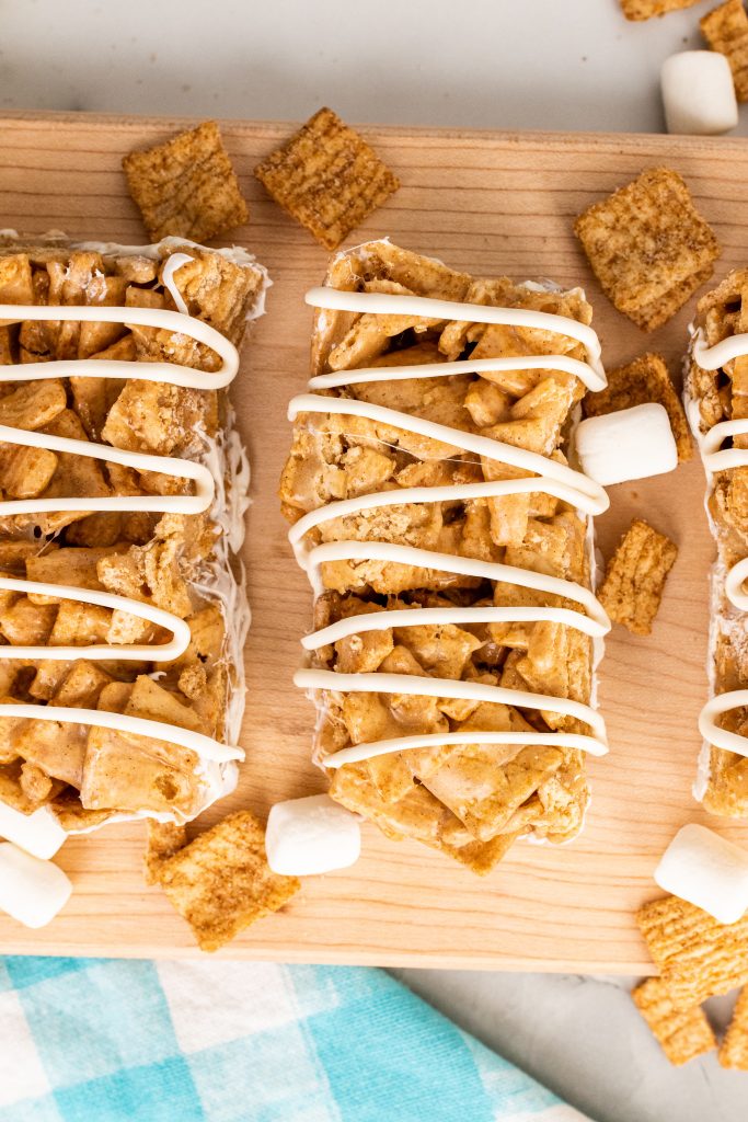 cinnamon toast crunch cereal bars drizzled with white chocolate arranged in a row on a wooden cutting board