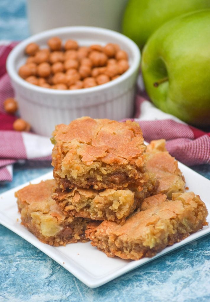 a stack of caramel apple blondies on a white square appetizer plate with whole apples in the background