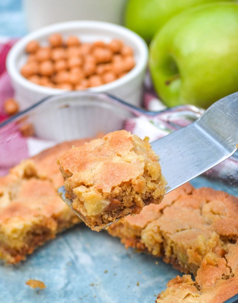 a silver server holding up a slice of caramel apple blondies above the baking dish