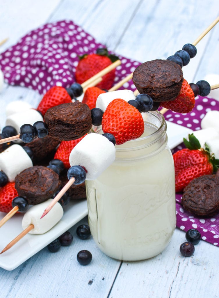 two different wooden skewers of dessert kabobs set overtop the rim of a glass of milk to form an X