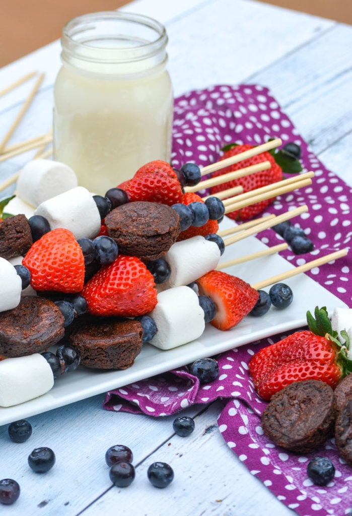 dessert kabobs shown stacked on a white platter next to a glass of milk