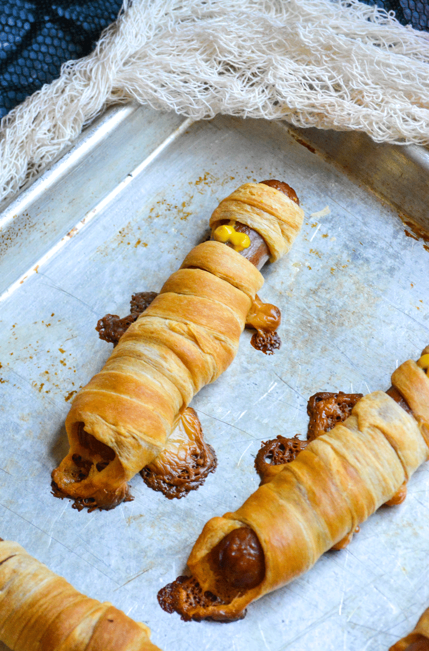 crescent roll wrapped mummy dogs on a metal sheet pan
