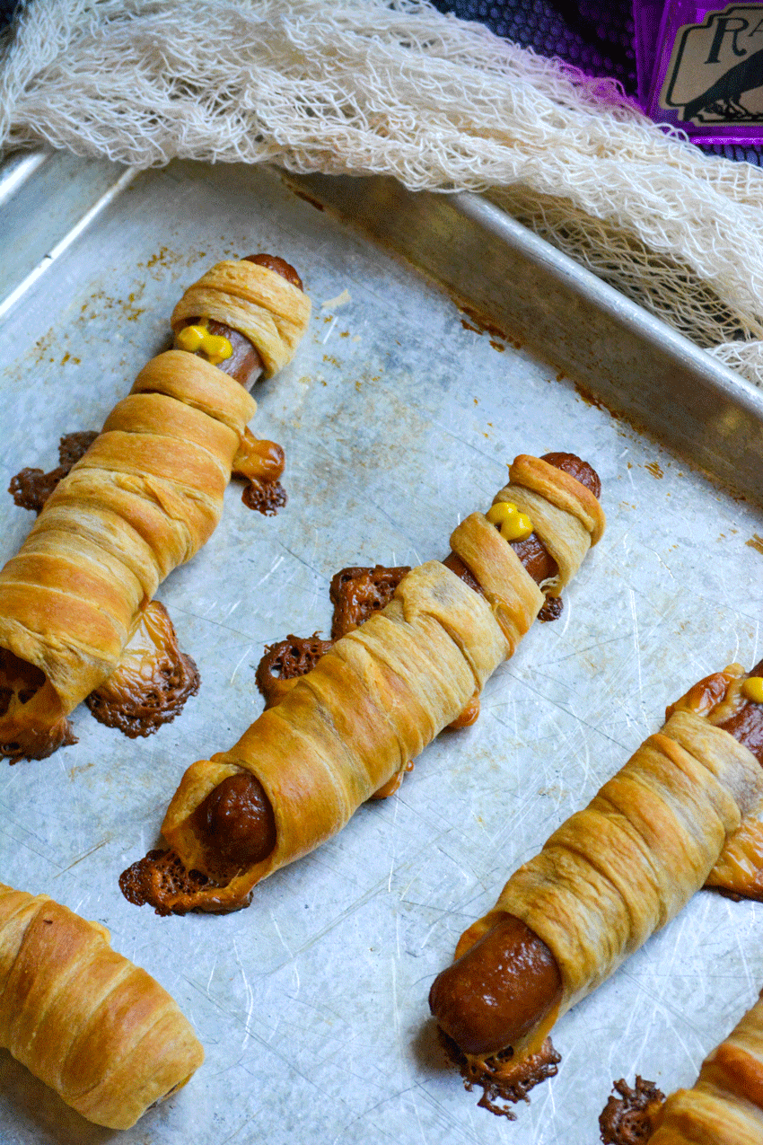 crescent roll wrapped mummy dogs on a metal sheet pan