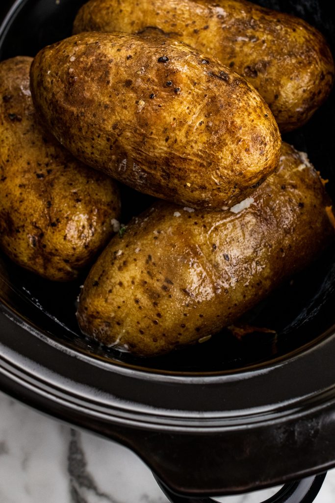 crock pot baked potatoes shown in the black bowl of a slow cooker