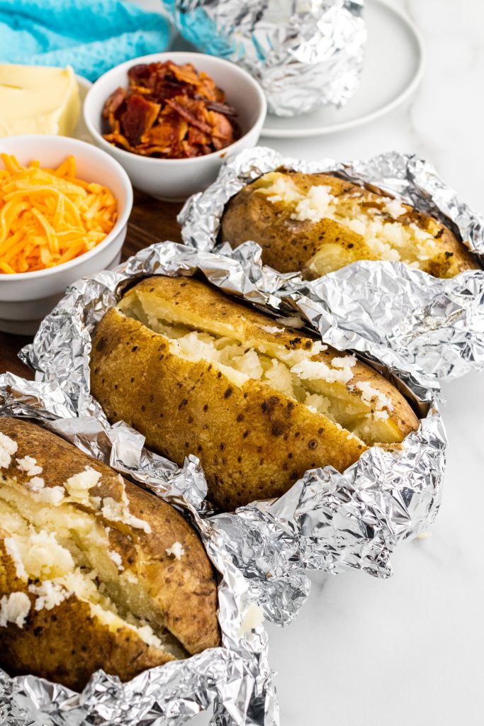 three crockpot baked potatoes sliced and ready for toppings
