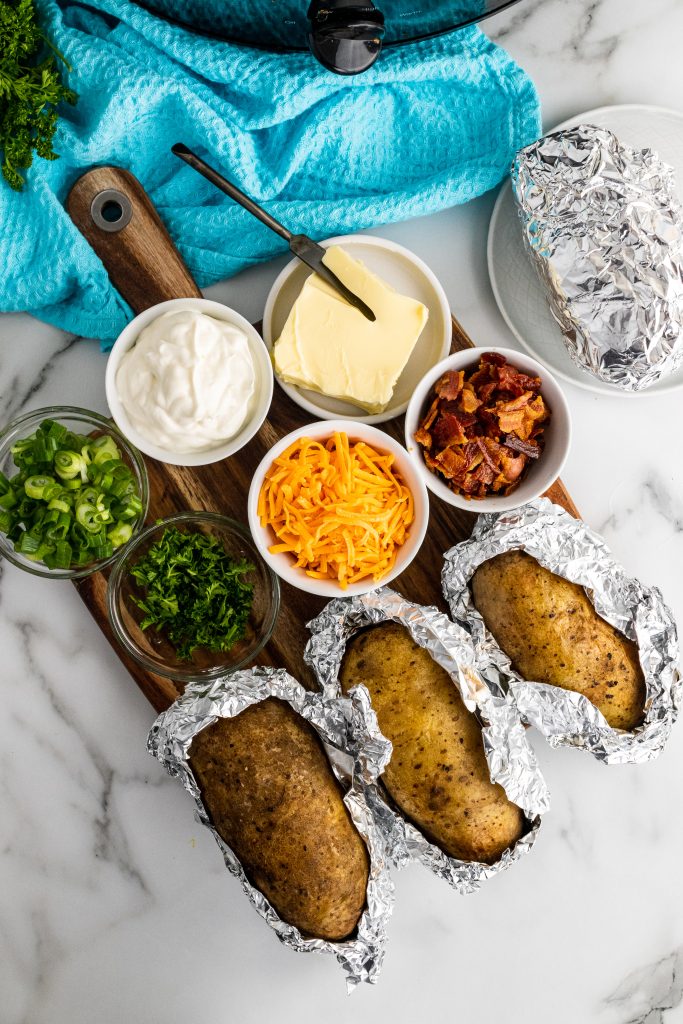 crock pot baked potatoes arranged on a cutting board with various bowls filled with topping options