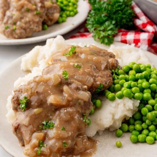 hamburger steaks with gravy and onions over mashed potatoes on a white plate