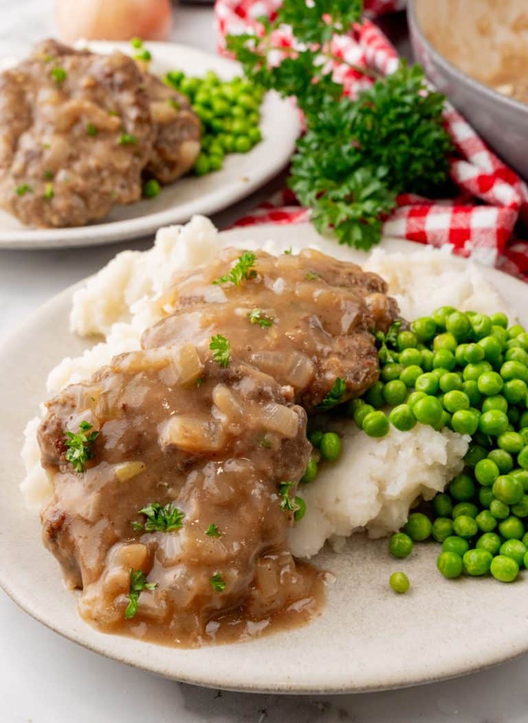 hamburger steaks with gravy and onions over mashed potatoes on a white plate