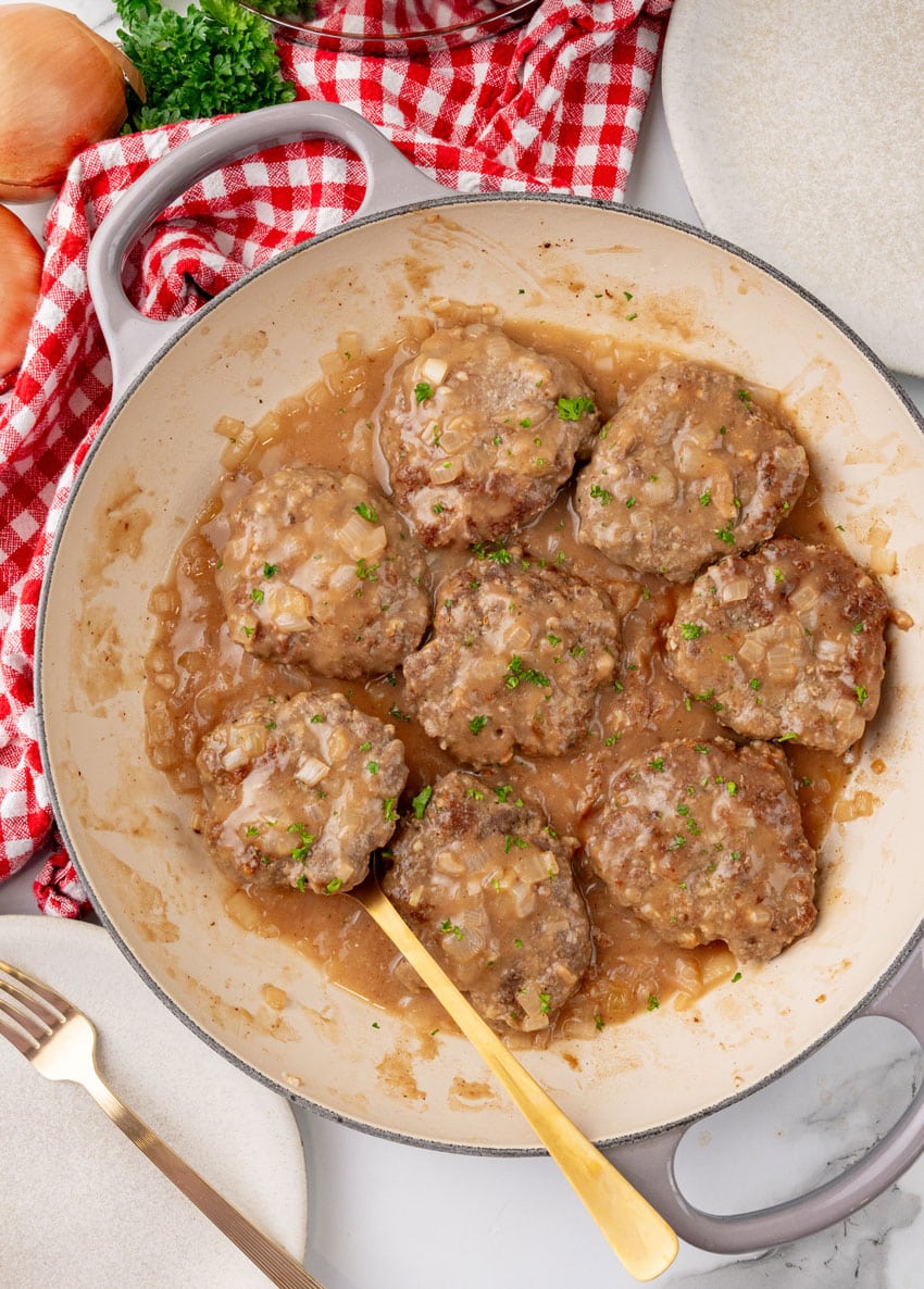 homemade hamburger steaks in onion gravy in a large cast iron skillet