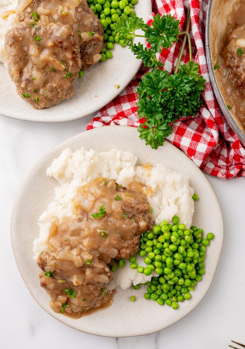 hamburger steaks with gravy and onions over mashed potatoes on a white plate