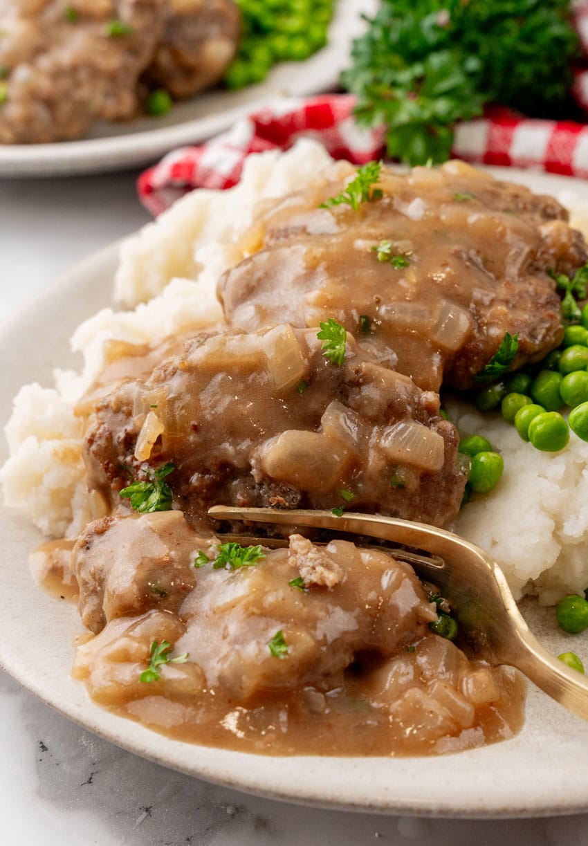 hamburger steaks with gravy and onions over mashed potatoes on a white plate