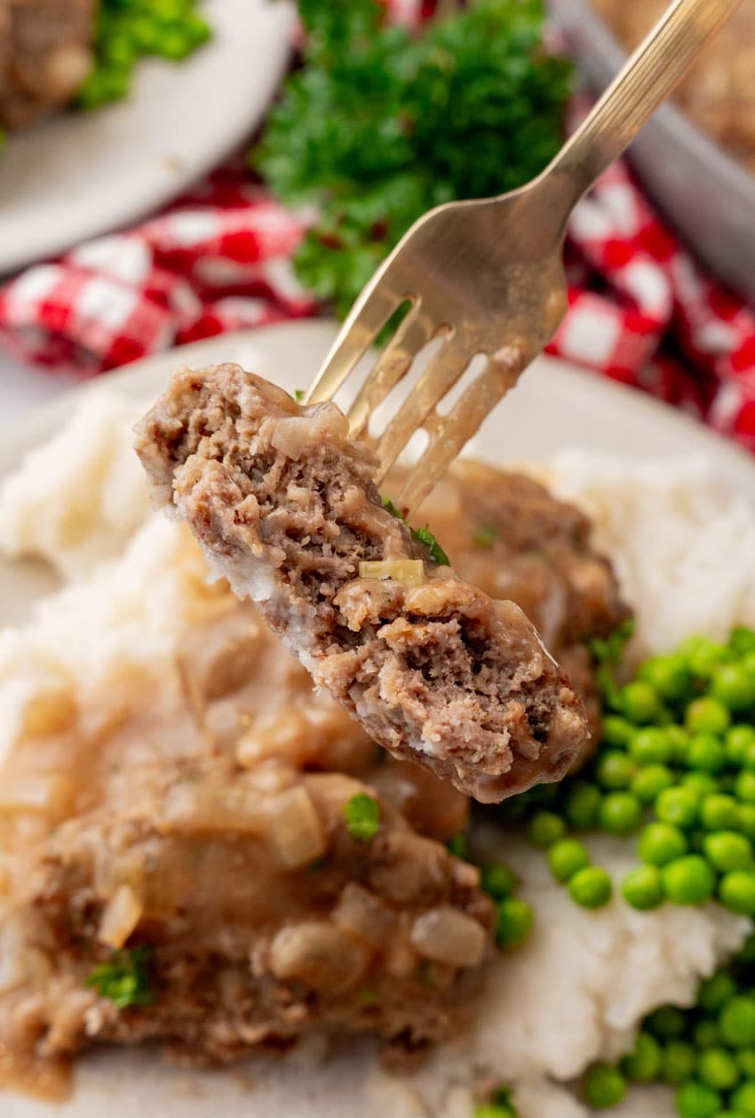 a fork holding up a slice of a homemade hamburger steak covered in onion gravy