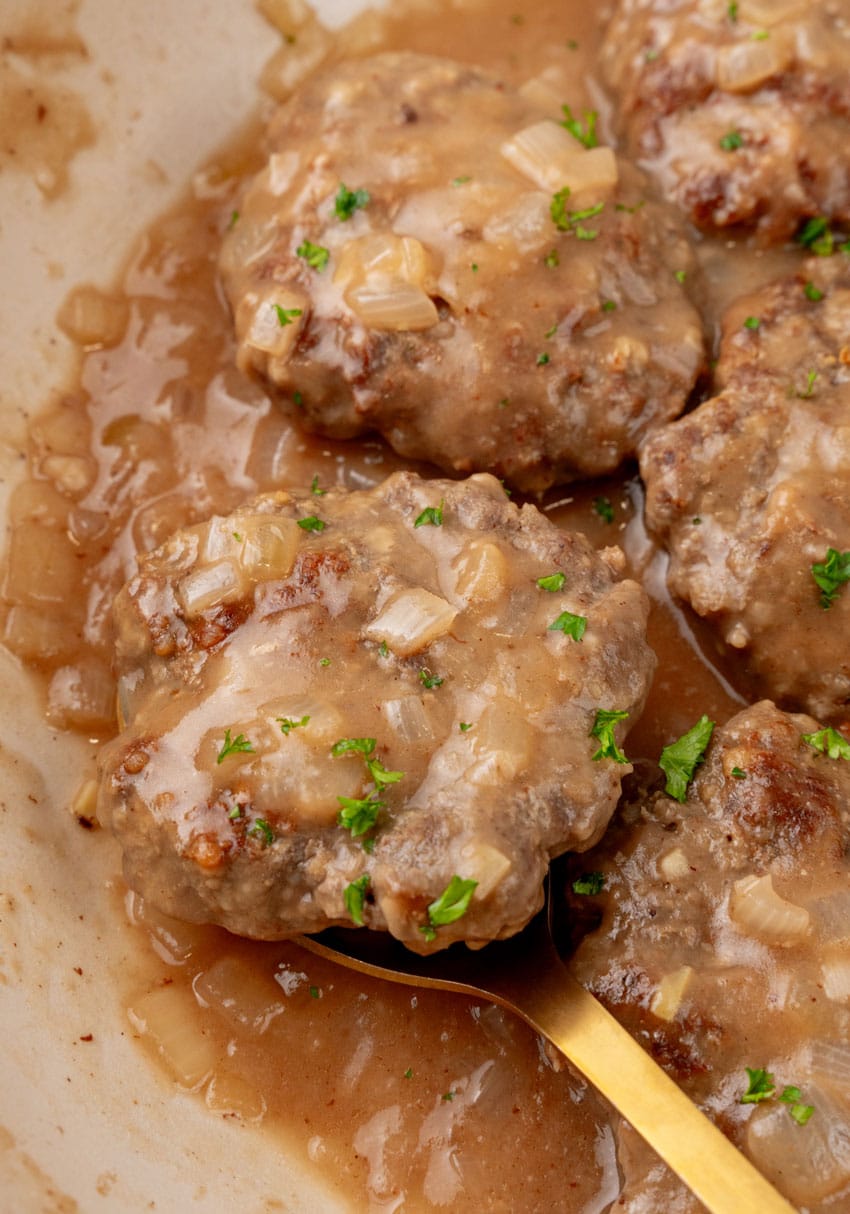 homemade hamburger steaks in onion gravy in a large cast iron skillet