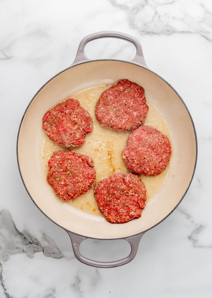 homemade hamburger steak patties in a large enameled cast iron skillet