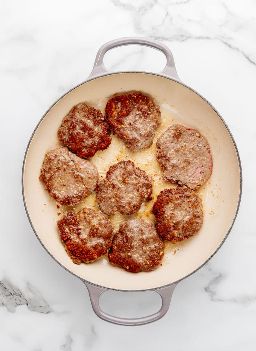 homemade hamburger steak patties frying in a large enameled cast iron skillet