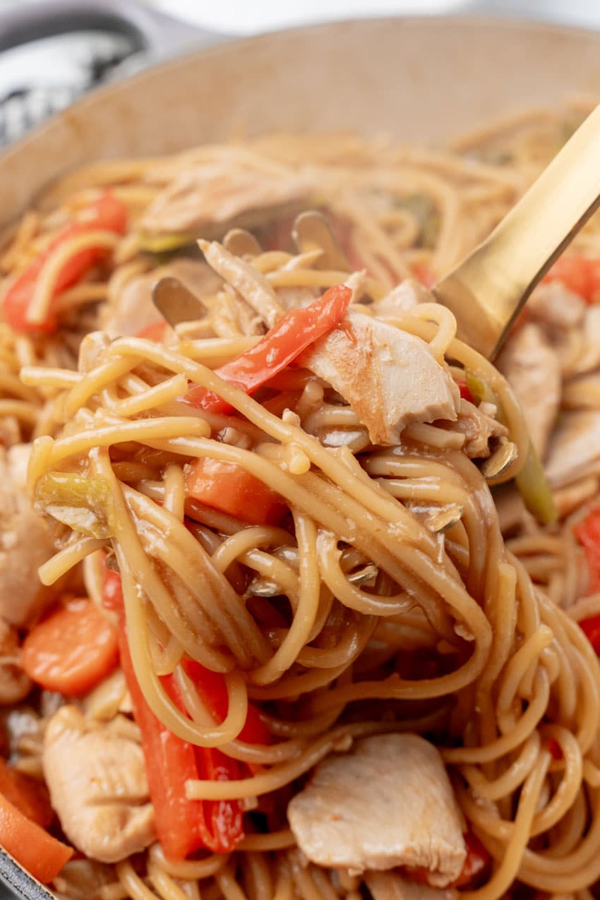 a golden scoop scooping one pot chinese lo mein pasta out of a cast iron skillet