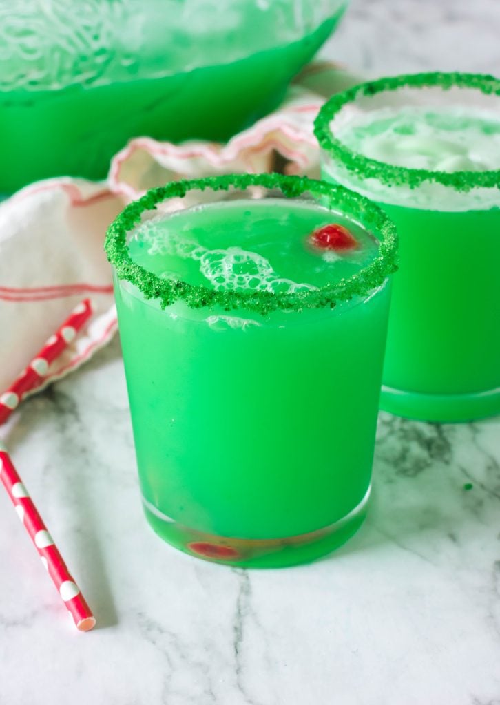 Christmas grinch punch served in green sugar rimmed glasses with a maraschino cherry floating in the green liquid