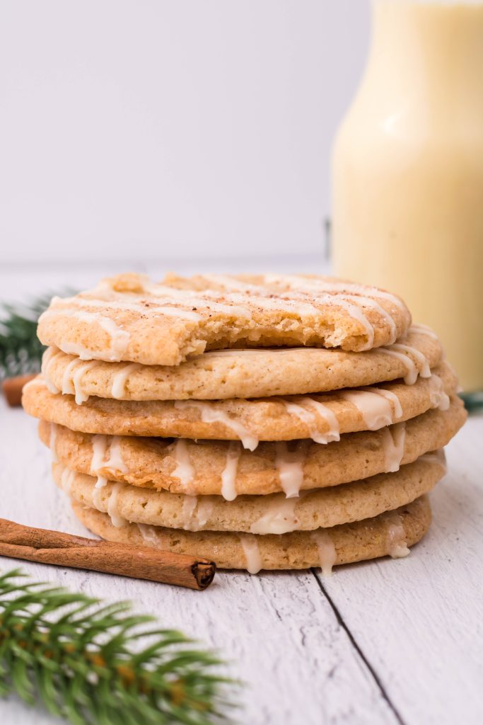 a stack of iced eggnog cookies in front of a glass of eggnog