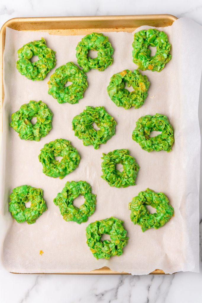 green marshmallow coated cornflakes wreaths arranged on a wax paper covered baking sheet