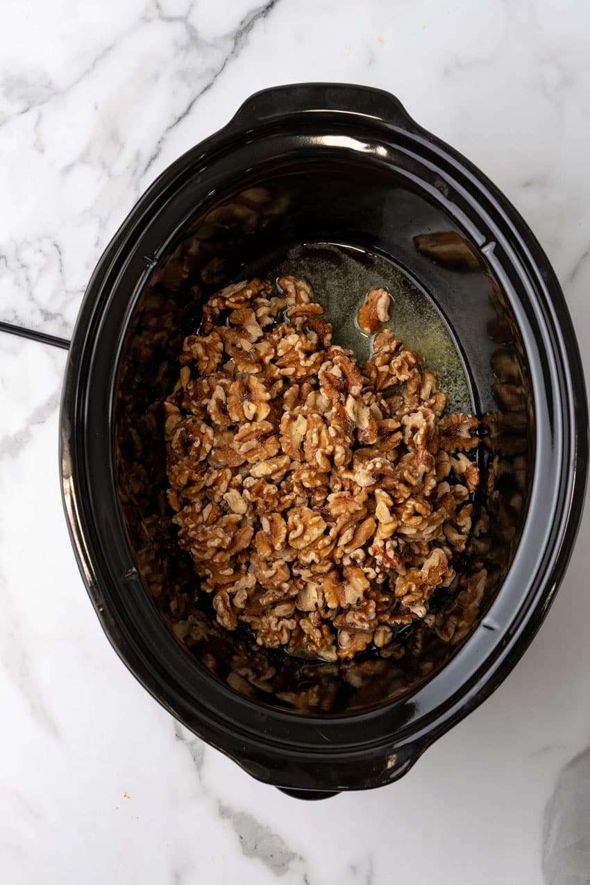 an overhead image showing walnuts, melted butter, and maple syrup in a black crock