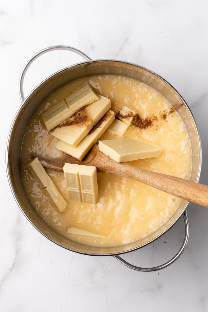 chunks of white chocolate and vanilla extract in a pan of eggnog fudge syrup