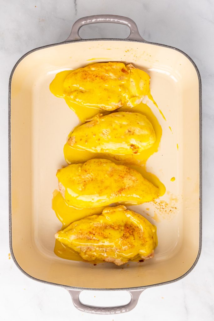 a row of honey mustard topped chicken breasts in a shallow casserole dish