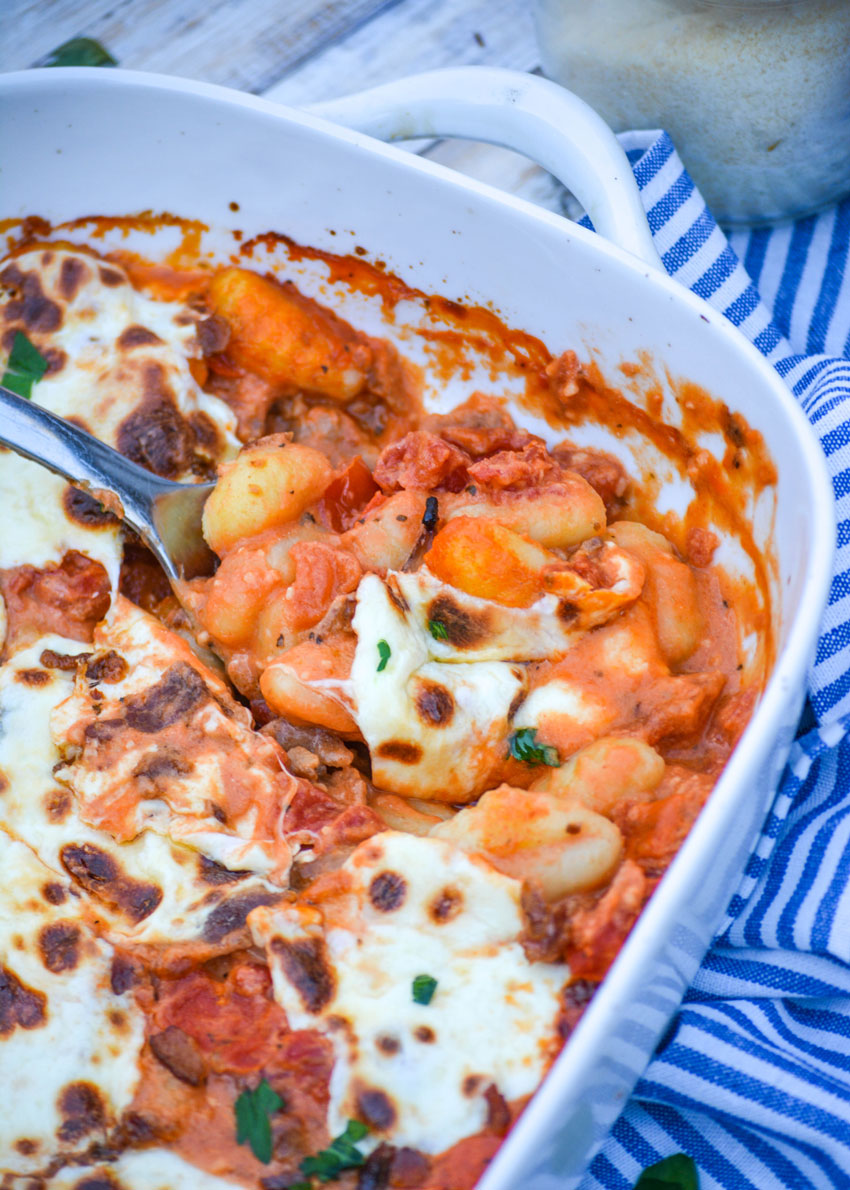 a silver spoon in a casserole dish filled with cheesy baked gnocchi