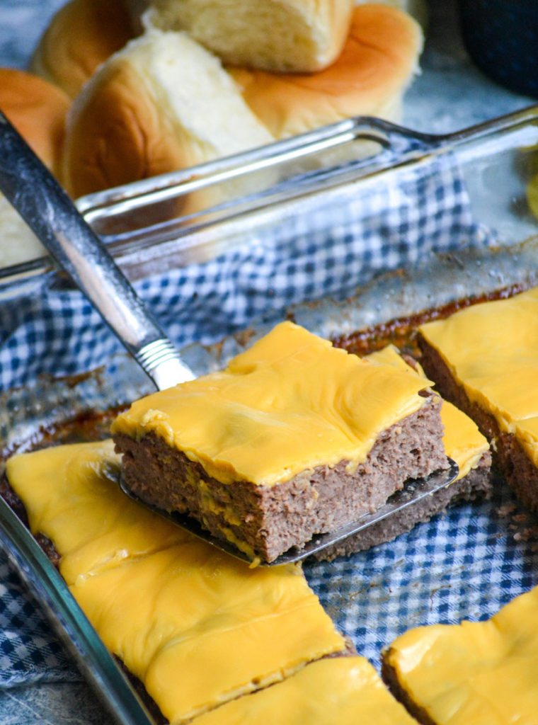 a silver spatula holding up a square shaped cheeseburger patty