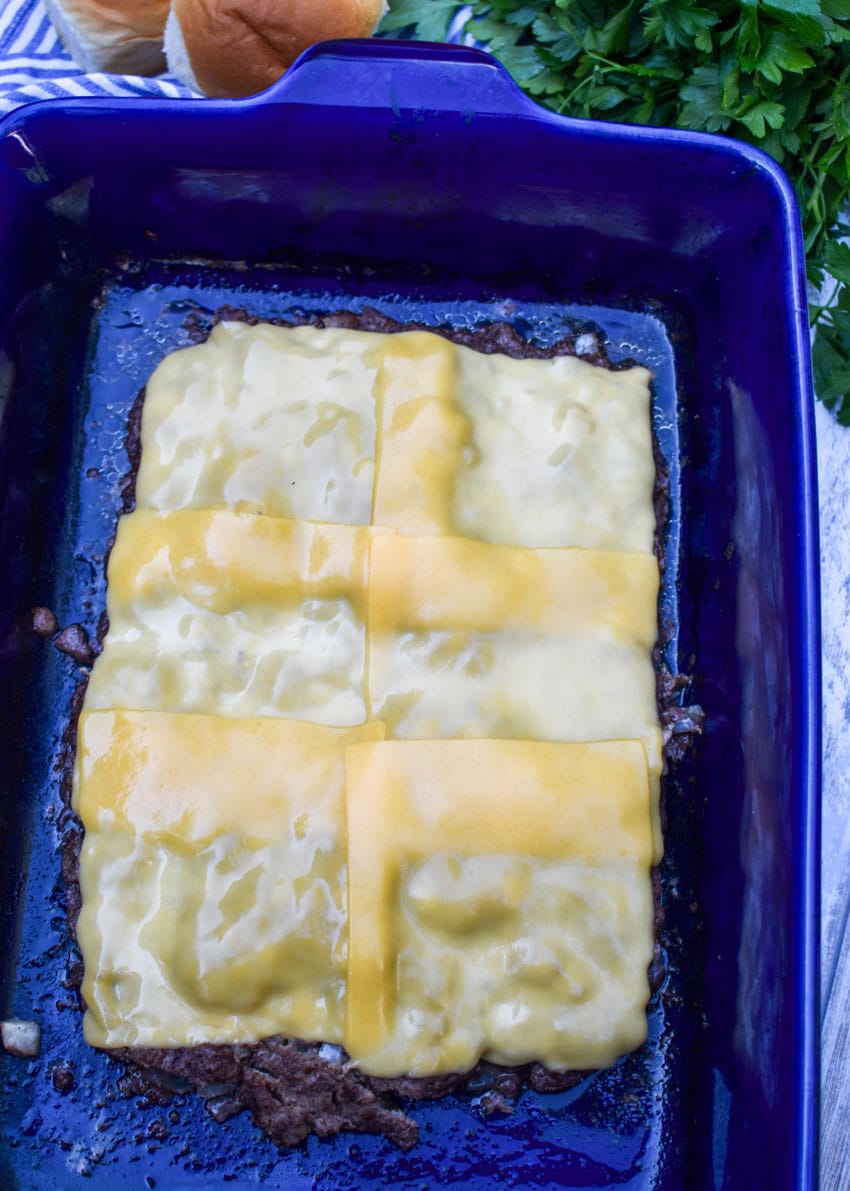 a large cheese topped rectangular cooked hamburger patty in a blue casserole dish