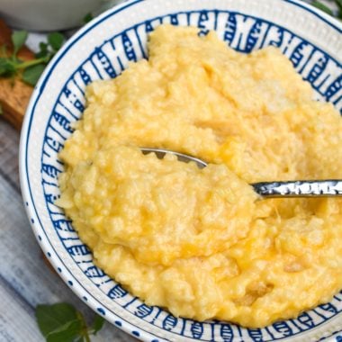 cheesy crock pot risotto in a blue and white bowl with a silver spoon
