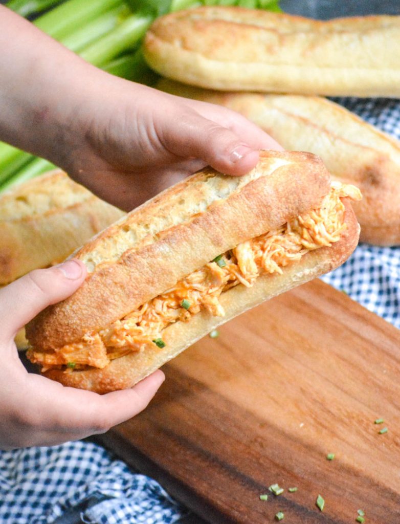 small hands holding up a pulled buffalo chicken sub sandwich