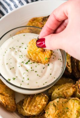 a hand dipping a crispy fried dill pickle chip in a bowl of ranch dressing