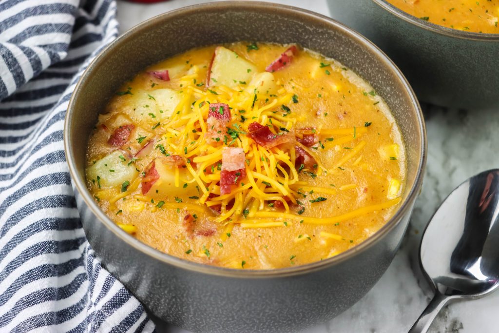 corn and potato studded smoky bacon and cheddar chowder shown in gray soup bowls topped with shredded cheddar cheese and crisp bacon bits