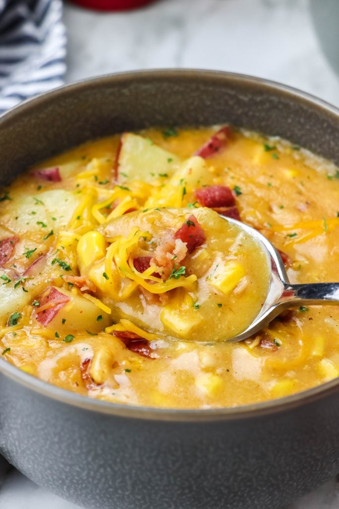 a silver spoon shown scooping up a spoonful of creamy, corn filled instant pot smoky bacon and cheddar chowder