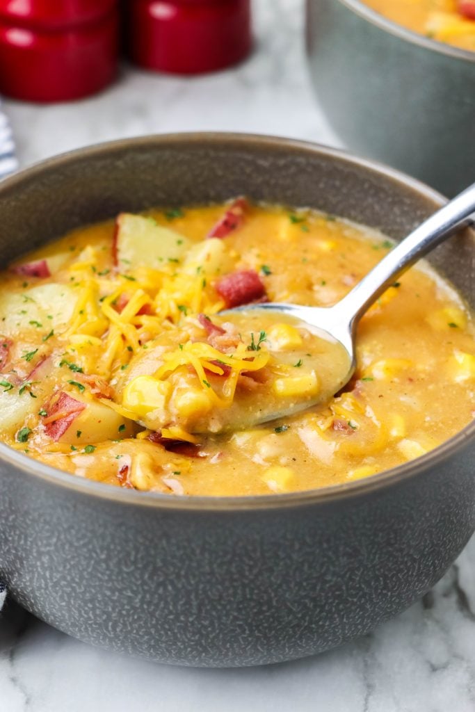 a silver spoon shown scooping up a spoonful of creamy, corn filled instant pot smoky bacon and cheddar chowder