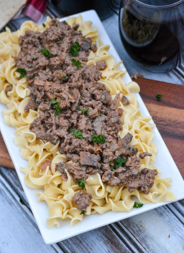 ground beef stroganoff served over top cooked egg noodles on a white rectangular platter