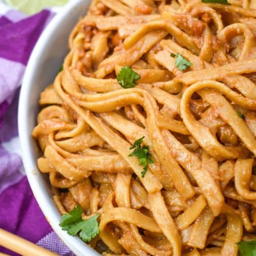 chinese peanut butter noodles in a white serving bowl with a pair of chop sticks on the side