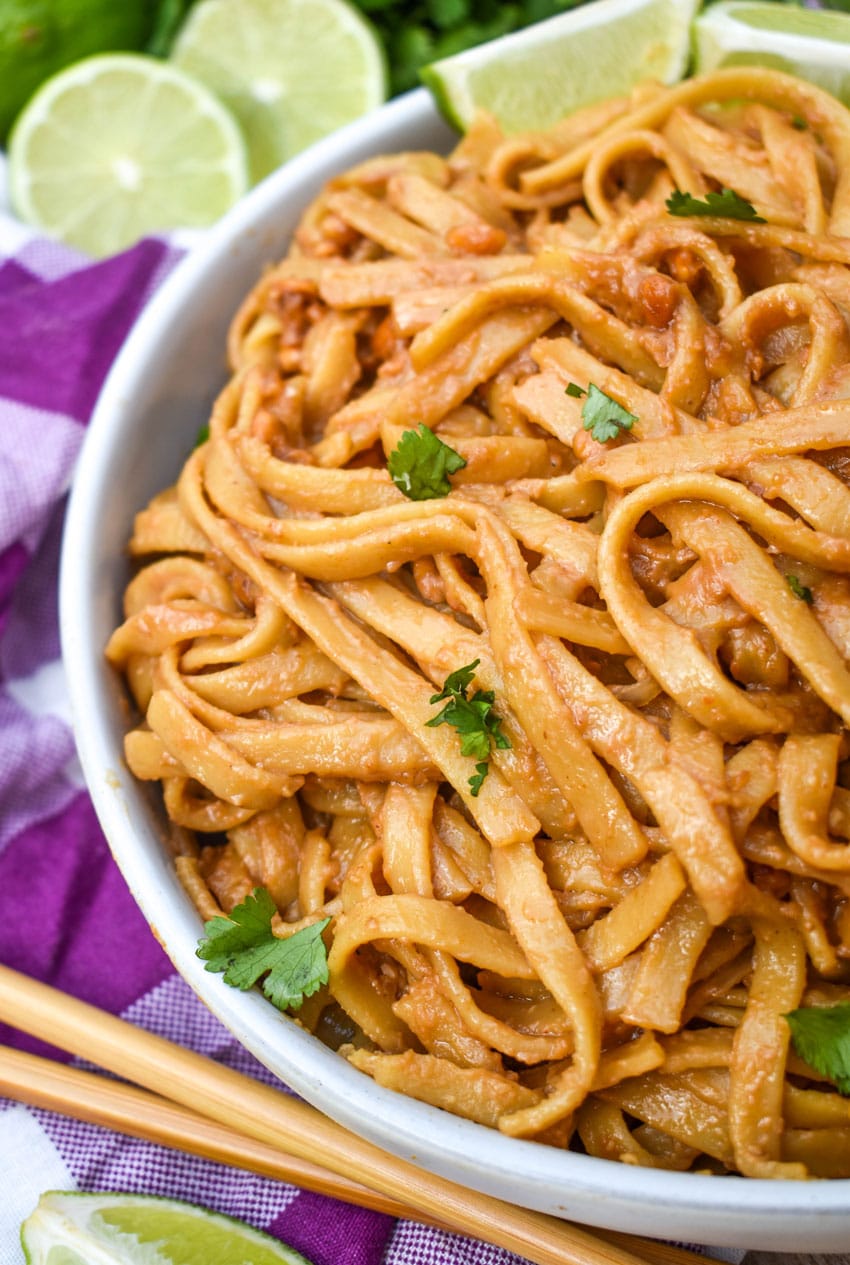 chinese peanut butter noodles in a white serving bowl with a pair of chop sticks on the side