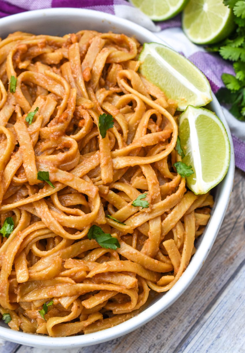 chinese peanut butter noodles in a white serving bowl with a pair of chop sticks on the side