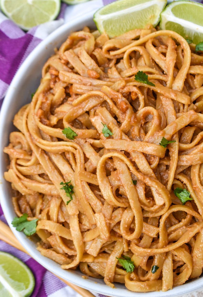 chinese peanut butter noodles in a white serving bowl with a pair of chop sticks on the side