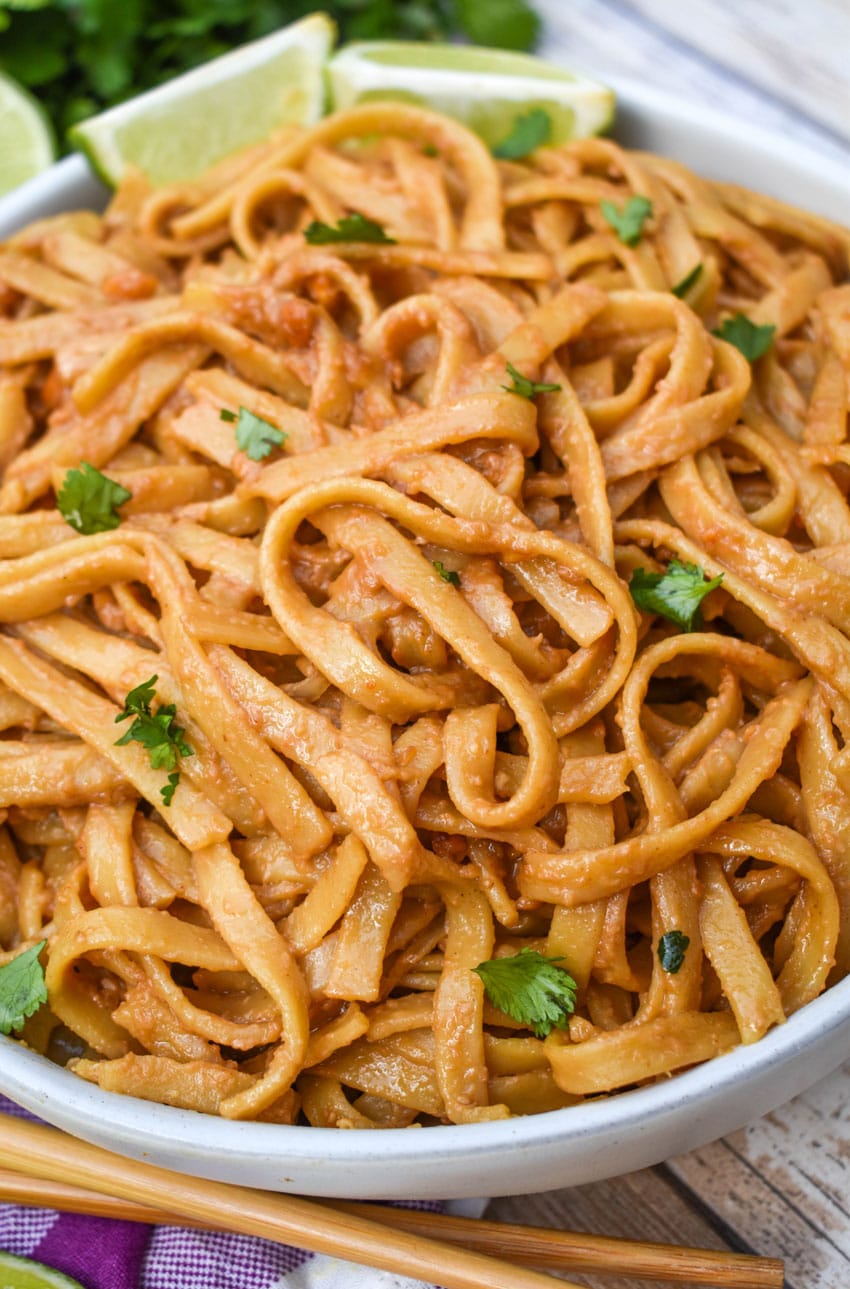 chinese peanut butter noodles in a white serving bowl with a pair of chop sticks on the side