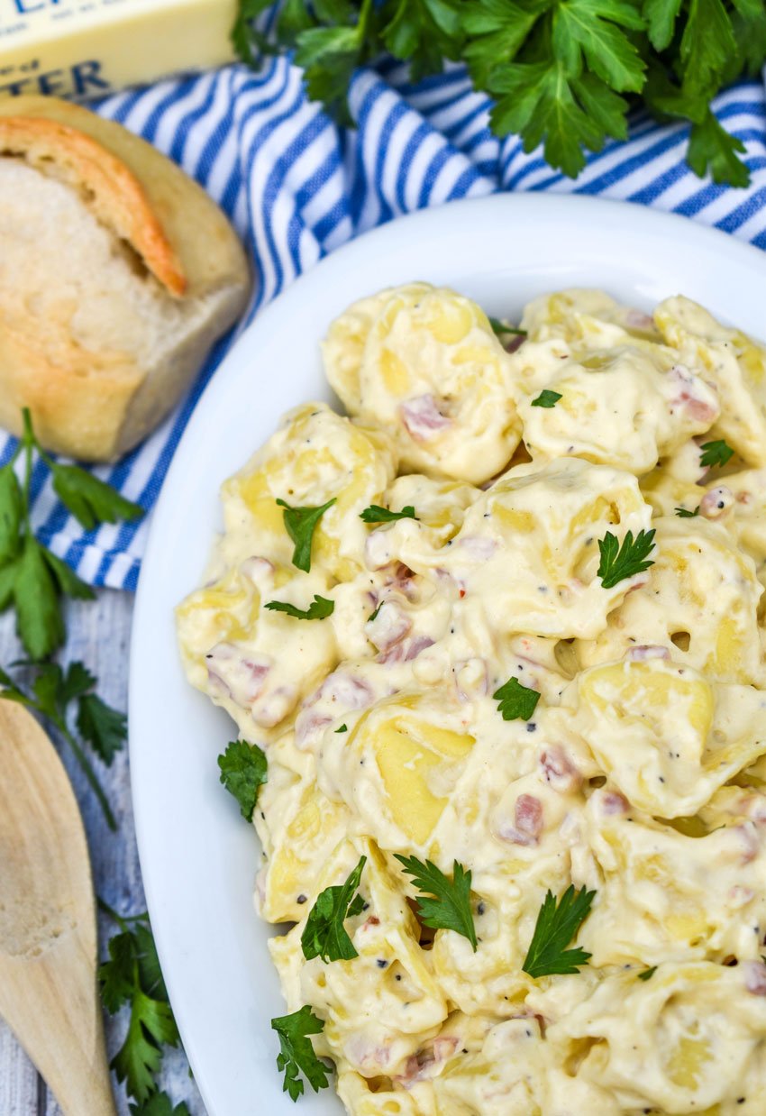 a white serving platter filled with creamy alfredo tortellini with ham topped with chopped fresh herbs