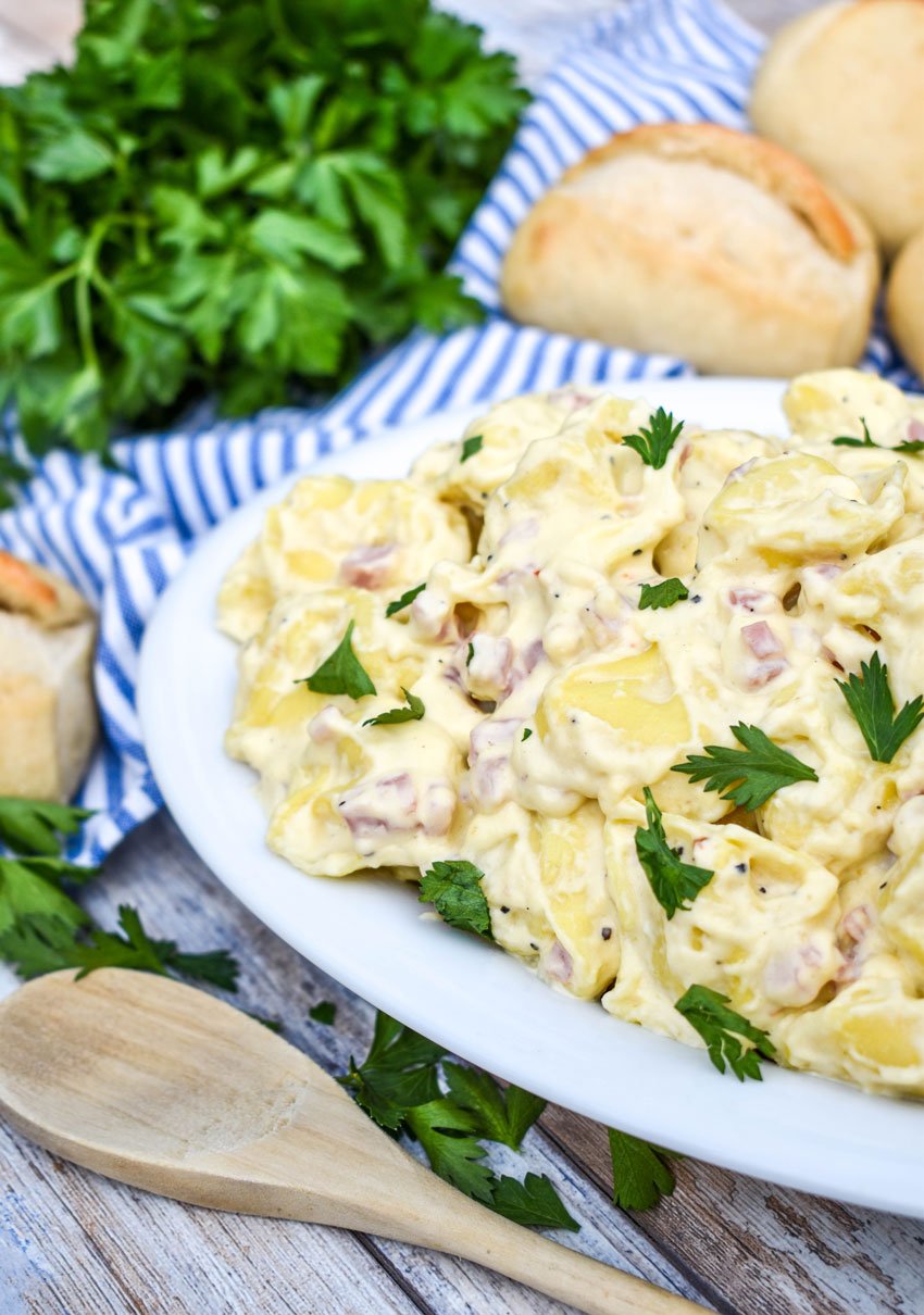 a white serving platter filled with creamy alfredo tortellini with ham topped with chopped fresh herbs
