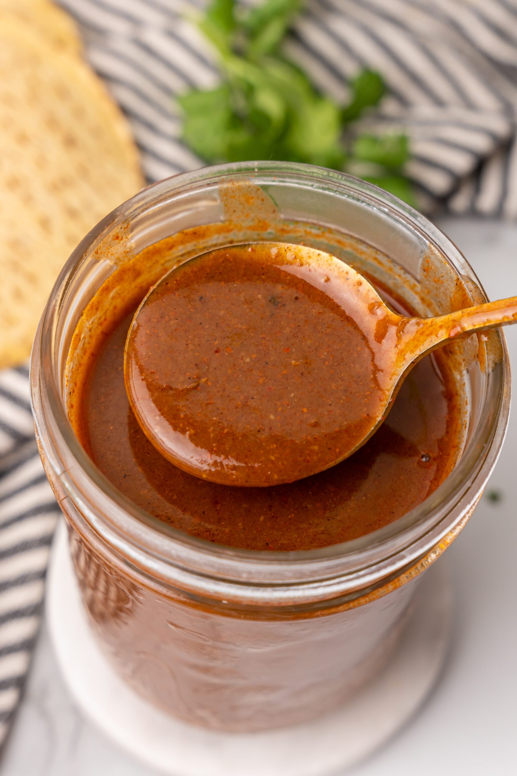 a golden spoon holding up a scoop of homemade enchilada sauce above a glass jar